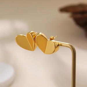 Detailed view of 18K gold heart-shaped stud earrings on a gold jewelry stand