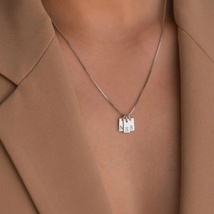 Detail shot of square letter pendants M S B on a fine box chain over a beige blazer