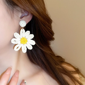 Close-up of handmade white and yellow woven daisy earrings on a model's ear