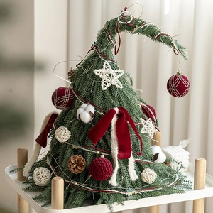 Mini sapin de Noël vert courbé avec nœuds rouges et pommes de pin sur étagère blanche
