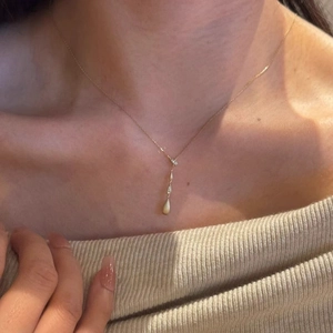 Macro shot of gold water-drop pendant necklace with zircon stones on a model's neck