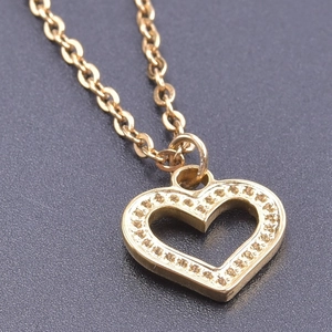 Close-up of golden stainless steel heart pendant with textured dotted edges on dark background