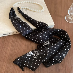 Detail showing polka dot fabric scarf intertwined with polished white pearls and floral pattern