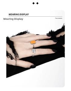 Close-up of feather textured silver ring and orange enamel ring on hand in gothic style