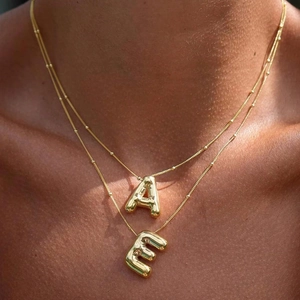 Layered gold bubble letter necklace with A and E pendants worn on a stylish neckline