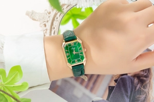 Macro shot of rectangular emerald dial with golden numerals and green leather strap