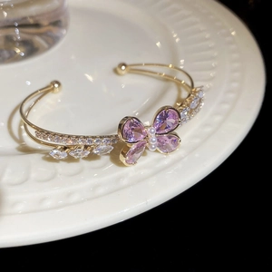 Macro shot of gold butterfly bracelet with purple stones and pearls on ceramic dish