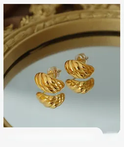 Close-up of golden ribbed horn earrings on mirror surface with vintage gold frame background