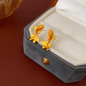 Détail macro de boucles d'oreilles carpe koi dorées mates sur boîte à bijoux en velours