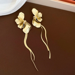 Gros plan sur des boucles d'oreilles fleurs dorées avec pétales texturés et longues chaînes