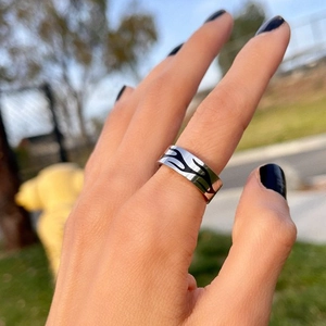 Detail of silver titanium steel ring with black flame pattern worn on hand outdoors