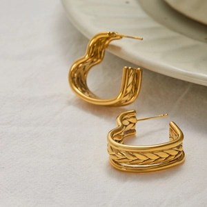 Close-up of 18K gold stainless steel earrings with braided heart-shaped texture on linen