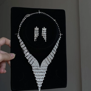 Detail of luxury V-shaped tassel necklace and earrings set with rhinestones on black stand