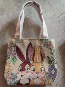 Detailed embroidery of cartoon rabbits and floral patterns on beige woven canvas bag