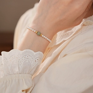 Close-up of pearl bracelet with green jade bead worn on wrist with lace sleeves