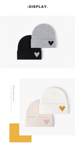 Detailed close-up of knitted winter beanie featuring contrast heart patch in four colors