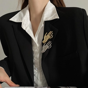 Detailed view of polished gold and silver palm brooches styled on a black blazer lapel
