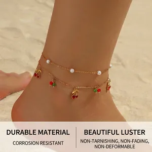 Double-layered golden anklet with cherry pendants and white pearls on beach