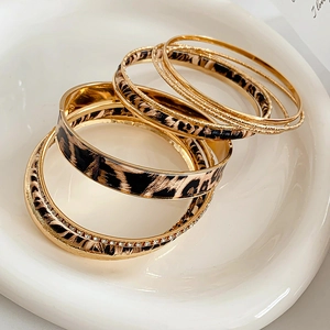 Close-up of stacked leopard print and gold-tone bracelets set in a white ceramic dish