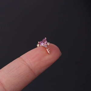 Detailed macro shot of a rose gold heart key cartilage earring held on a fingertip