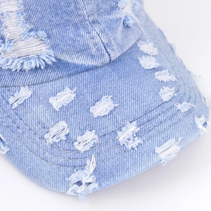 Close-up detail of vintage washed blue denim baseball cap with distressed ripped textures