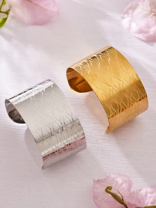 Détail de bracelets manchettes ondulés dorés et argentés sur fond en bois blanc