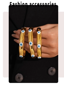 Detailed view of three 18k gold plated evil eye open bangles held against black fabric