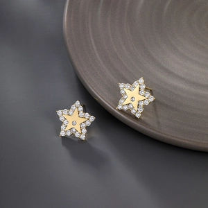 Close-up of star shaped gold earrings with clear cubic zirconia on grey background