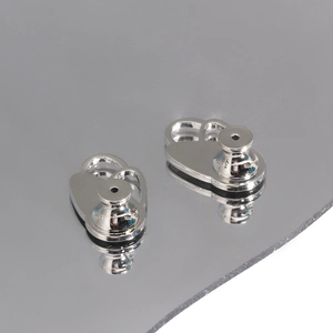 Macro detail of silver-finish earring lifters with back supports on reflective surface