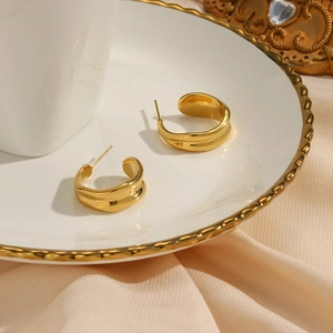 Detail of 18K gold plated wavy C-shaped earrings on cream silk and vintage ceramic
