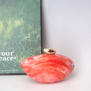 Detail of red marble texture acrylic evening clutch with gold metal clasp and glossy finish