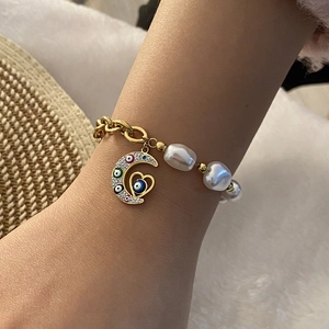 Detail of gold chain bracelet with baroque pearl and evil eye crescent moon charm