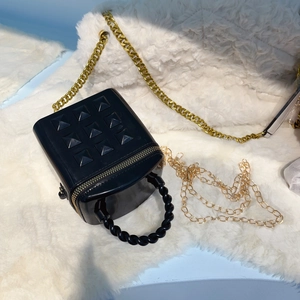 Top view of mini black studded bucket bag with golden chain on white plush background