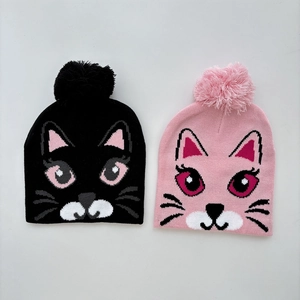 Detail of two-piece girls knitted cat hats with fluffy pompoms and jacquard patterns