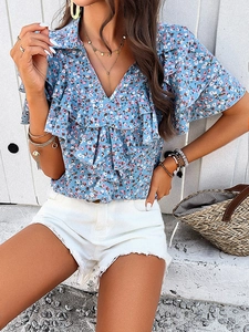 Detail of elegant V-neck floral blouse with blue ruffles and white shorts