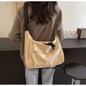 Detail of beige canvas tote bag with adjustable black strap worn by a model in a cafe