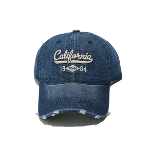 Detail of distressed denim baseball cap with California 1984 embroidery and frayed brim