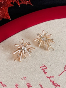 Macro shot of gold firework stud earrings with white enamel heart and sparkling crystals