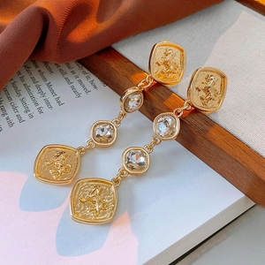 Close-up of vintage golden lion crest earrings with crystals on a warm textured background