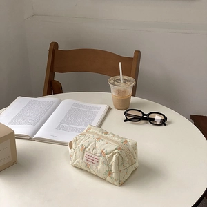 Detailed close-up of a floral quilted cotton cosmetic bag on a white table with props