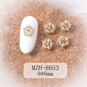 Macro detail of 8x8mm gold snowflake nail charms with crystal rhinestone on white nails