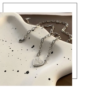 Detail of silver heart necklace with Never Forget engraving on a ceramic plate