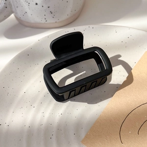 Detail shot of a matte black square hair claw clip on a minimalist ceramic plate