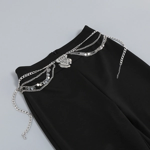 Detail of silver multi-layer metal waist chain with triangle pendant on black trousers