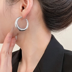 Close-up of polished silver C-shaped hoop earrings worn by a model in a minimalist style