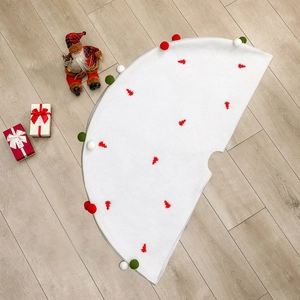 Jupe de sapin de Noël blanche en peluche avec motifs rouges et pompons sur sol en bois