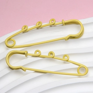 Detail view of two large yellow metal safety pins on a soft pink and white background
