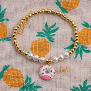 Detail of beaded bracelet featuring gold beads, pearls, and a pink donut charm