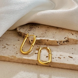 Detail of 18K gold-plated U-shaped earrings on beige stone and white silk fabric