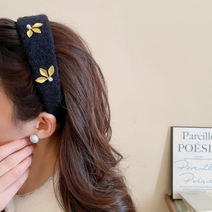 Detail of wide black velvet headband featuring golden metal leaves and white faux pearls